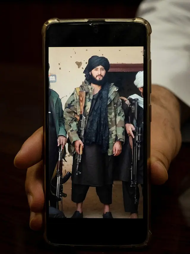 Foto yang diambil pada 18 Januari 2022 ini menunjukkan Wali Kota Maymana Damullah Mohibullah Mowaffaq memegang ponselnya dengan foto dirinya saat menjadi pejuang Taliban, di Maymana. (AFP)