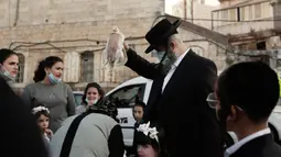 Seorang pria Yahudi ultra-Ortodoks mengayunkan ayam di atas kepala keluarganya sebagai bagian dari ritual Kaparot di Yerusalem, Rabu (23/9/2020). Tradisi itu digelar sebelum perayaan Yom Kippur atau hari Penebusan dosa, hari paling suci dalam tahun Yahudi. (AP Photo/Maya Alleruzzo)
