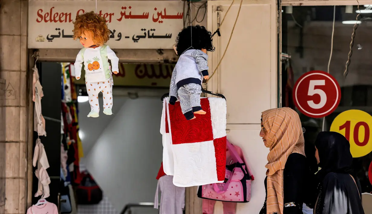 Wanita Palestina berjalan melewati boneka di luar toko pakaian bayi di pasar di kota tua Betlehem di Tepi Barat yang diduduki (14/9/2021).  Ekonomi Palestina diperkirakan akan tumbuh empat persen pada tahun 2021 setelah terpukul pada tahun 2020 akibat pandemi COVID-19. (AFP/Emmanuel Dunand)