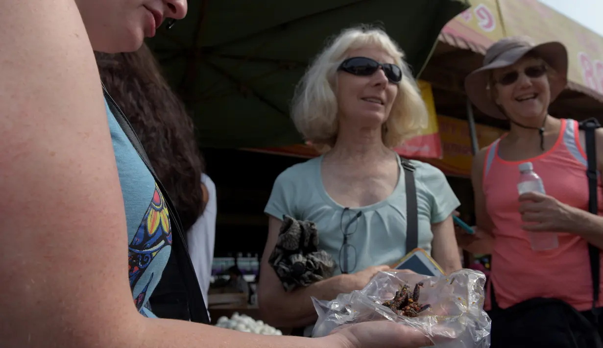 Wisatawan memegang camilan tarantula goreng di wilayah Skun, Provinsi Kampong Cham, Kamboja, 14 Maret 2018.  Harga tarantula melonjak hingga Rp 13.700 per ekor, meningkat hampir 10 kali lipat selama satu dekade terakhir. (TANG CHHIN Sothy / AFP)