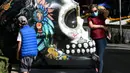 Seorang anak dan perempuan berada di samping tengkorak yang dihias selama pameran edisi keempat "Mexicraneos" (Mexisculls) di Reforma Avenue, Mexico City pada 23 Oktober 2020. Pameran itu karya seniman dari berbagai bagian negara Meksiko, juga Amerika Serikat dan Venezuela. (ALFREDO ESTRELLA/AFP)
