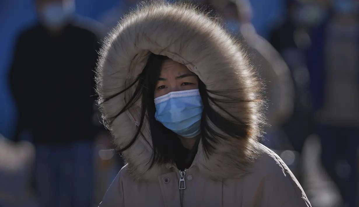Seorang wanita mengenakan masker untuk membantu mengekang penyebaran virus corona bersiap menghadapi angin dingin saat dia berjalan di dekat distrik perbelanjaan Wangfujing di Beijing, Minggu (12/12/2021). (AP Photo/Andy Wong)