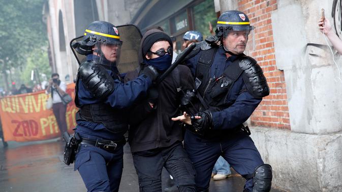Polisi anti huru-hara mengamankan seorang demonstran saat terjadi bentrokan di Paris, Prancis (23/5). Mereka memprotes kebijakan pemerintah terkait pemangkasan 120.000 pekerjaan pada 2022. (AP/Christophe Ena)