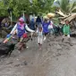 Orang-orang berjalan di tengah puing-puing di sebuah desa yang terkena banjir di Ile Ape, di Pulau Lembata, provinsi Nusa Tenggara Timur, Minggu (4/5/2021).  sejumlah ruas jalan dan jembatan rusak akibat banjir bandang tersebut. . (AP Photo/Ricko Wawo)