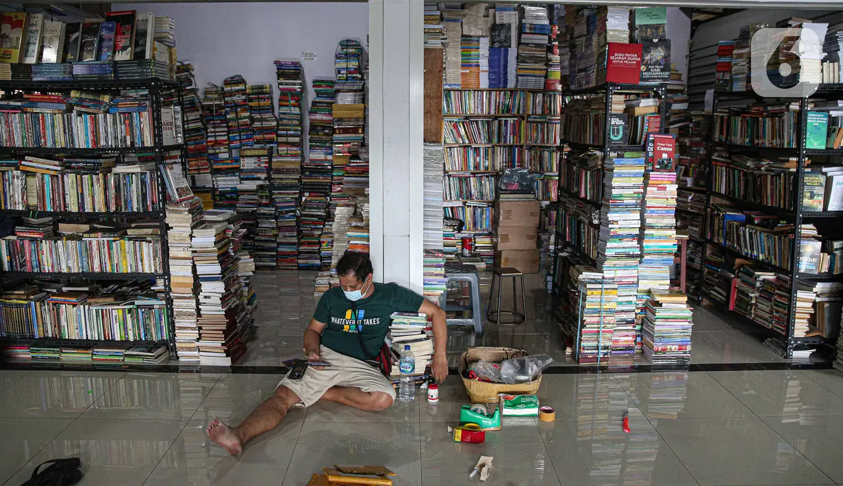 Pedagang bermain ponsel saat menunggu pembeli buku di Pasar Kenari, Jakarta, Rabu (24/11/2021). Sedangkan penjual hanya membayar keamanan dan listrik. Penjualan sangat sepi terdampak sekali pandemi, turun drastis hingga 80% yang sebelum pandemi bisa menjual 20 buku. (Liputan6.com/Faizal Fanani)