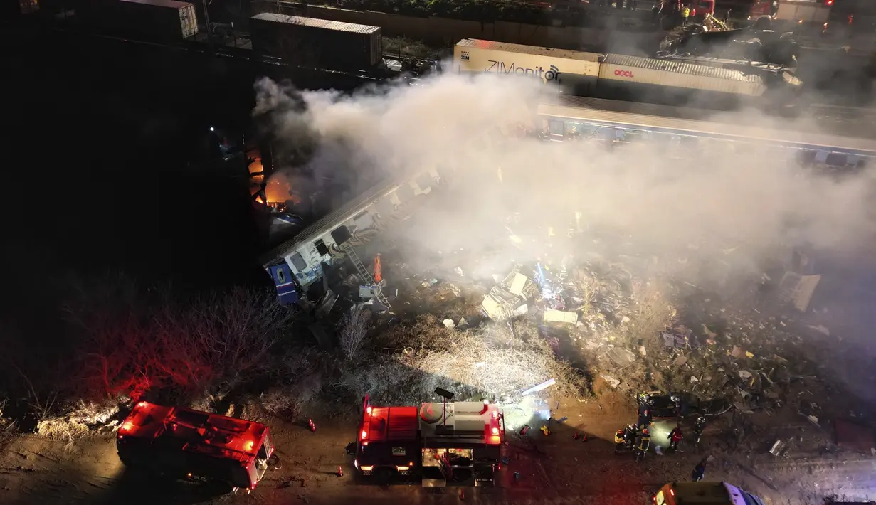 Asap mengepul dari kereta saat petugas pemadam kebakaran dan penyelamat beroperasi setelah tabrakan di dekat kota Larissa, Yunani, Rabu dini hari (1/3/2023). Tim penyelamat tengah bekerja untuk menyelamatkan penumpang dan memadamkan api. (AP Photo/Vaggelis Kousioras)