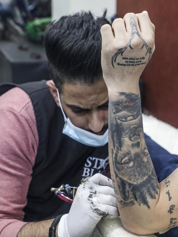 Naim Abdallah saat membuat desain tato pada lengan seorang klien di ruang kerjanya di Kota Betlehem, Tepi Barat (24/1/2021). Naim Abdallah merupakan salah satu seniman tato Palestina yang mempunyai bakat dan keahlian membuat tato dengan detail gambar yang sempurna. (AFP/Hazem Bader)