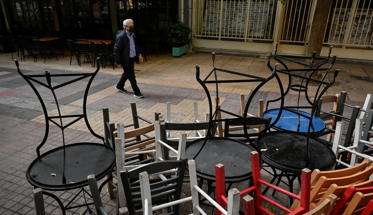 Seorang pejalan kaki berjalan melewati kafe-kafe yang tutup di pusat kota Athena, Yunani, Selasa (16/11/2021). Pemilik restoran, kafe, dan bar melakukan pemogokan selama 24 jam, memprotes aturan terkait Covid-19 dan biaya energi yang tinggi. (Sakis MITROLIDIS / AFP)