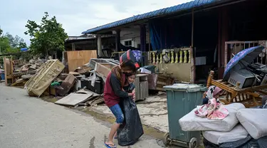 Seorang wanita memeluk anak di dekat puing-puing dan barang-barang di luar rumah mereka, setelah banjir surut di Mentakab, negara bagian Pahang Malaysia (11/1/2021). Banjir yang melanda daerah tersebut, membuat  Puluhan ribu warga dievakuasi. (AFP/Mohd Rasfan)