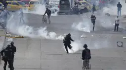 Seorang demonstran dan seorang polisi saling menendang tabung gas air mata saat protes antipemerintah di Bogota, Kolombia, Senin (28/6/2021). Protes dipicu oleh usulan kenaikan pajak atas layanan publik, bahan bakar, upah dan pensiun. (AP Photo/Fernando Vergara)