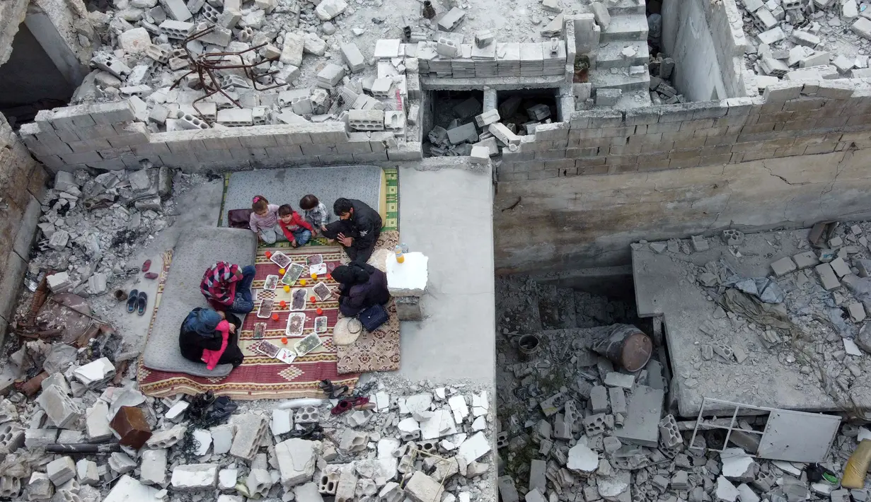 Keluarga Tareq Abu Ziad menunggu waktu berbuka puasa di tengah reruntuhan rumah mereka yang hancur setelah serangan militer pasukan pemerintah dan sekutunya di Kota Ariha, Provinsi Idlib, Suriah, Senin (4/5/2020). Muslim Suriah melewati Ramadan tahun ini masih dalam kondisi perang. (AAREF WATAD/AFP)