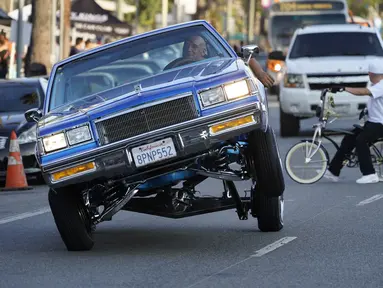 Sebuah mobil Lowrider melaju saat beratraksi dengan roda tiga di Sunset Boulevard, di lingkungan Echo Park, Los Angeles, pada 18 Juli 2021. Lowrider merupakan gaya dari kendaraan modifikasi yang bermula dari Los Angeles pada pertengahan hingga akhir 1940-an. (AP Photo/Damian Dovarganes)