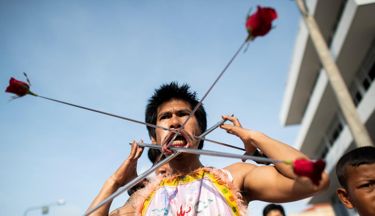 Penganut kuil Loem Hu Thai Su manusukkan batang besi panjang ke pipinya saat festival vegetarian tahunan di Phuket, Thailand, Jumat (12/10). Festival vegetarian ini sudah ada sejak tahun 1825. (Jewel Samad/AFP)