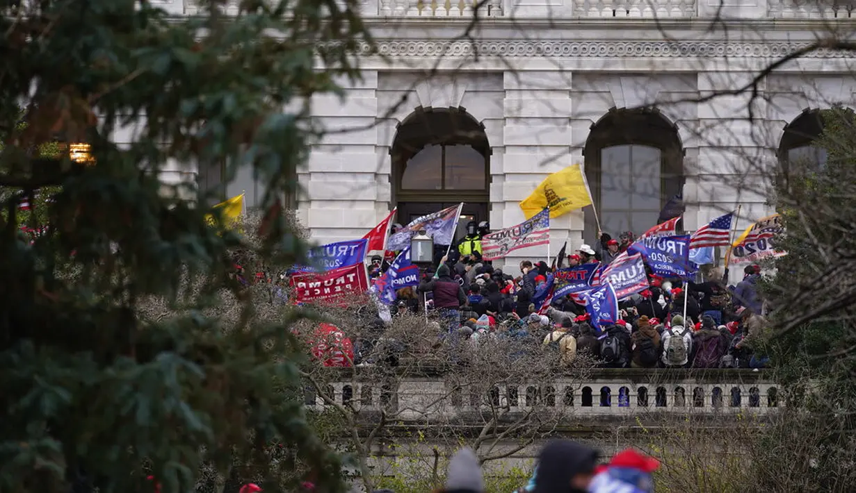 Massa pendukung Presiden Amerika Serikat Donald Trump tiba di pintu masuk samping Capitol Hill, Washington, Amerika Serikat, Rabu (6/1/2021). Sejumlah polisi DC pun jadi korban, mereka dibawa ke rumah sakit setelah terkena semprotan merica. (AP Photo/Julio Cortez)