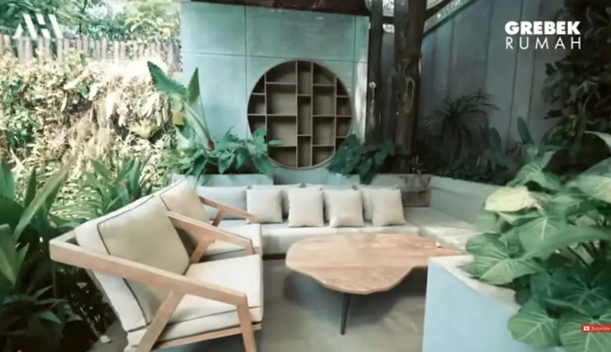 Tempat santai di halaman belakang, yang juga menggunakan meja kayu. Tidak jauh dari tempat ini juga ada meja dan kursi dengan kayu tebal. Rumahnya menjadi asri karena ia dan ibunya suka tanaman. [Youtube/AH]
