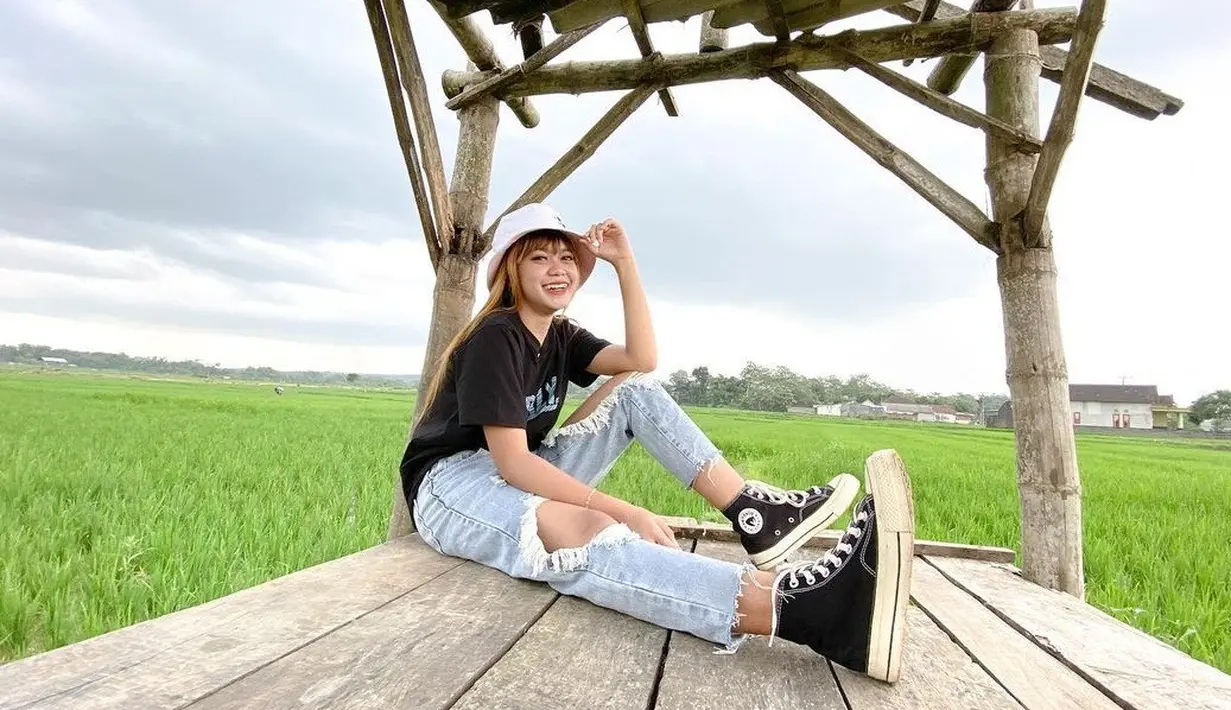 Palantun lagu "Gulu Pedot" ini berhasil beberapa kali trending di YouTube dengan musik videonya. Penampilannya tetap stylish saat berfoto di area sawah. Menggunakan bucket hat berwarna putih, baju kaus hitam dan celana jeans berwarna terang melengkapi gayanya. (Liputan6.com/IG/@esaristyyy_)