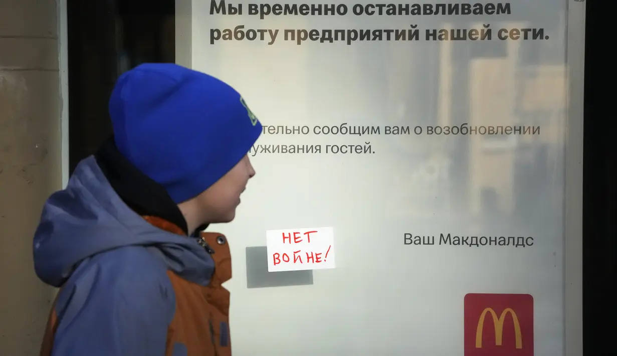 Seorang anak melewati tanda 'No War!' yang menempel di jendela restoran McDonald's dengan pemberitahuan penutupan restoran di St. Petersburg, Rusia, Selasa (15/3/2022). Gerai makanan siap saji McDonald's resmi menutup 850 gerainya yang beroperasi di Rusia pada 14 Maret 2022. (AP Photo)