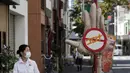 Seorang wanita mengenakan masker untuk membantu mencegah penyebaran virus corona berjalan melewati orang-orangan sawah yang menggambarkan tangan besar dengan tanda berhenti virus Corona di Tokyo, Senin (28/9/2020). Jepang mengonfirmasi lebih dari 70 kasus virus corona. (AP Photo/Eugene Hoshiko)