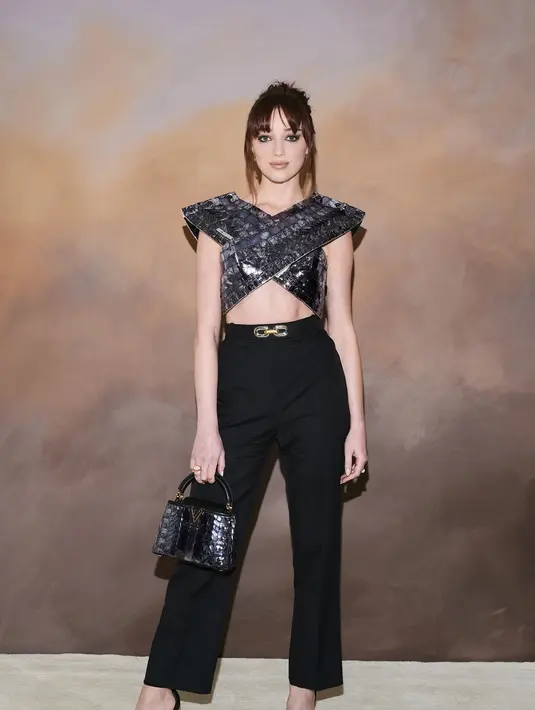 Phoebe Dynevor juga tampil cantik dengan atasan berpotongan crop top yang unik, dengan celana panjang hitam, open toe, dan handbag hitam. Foto: Document/Louis Vuitton.