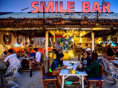 Orang-orang duduk di sebuah bar , saat para turis memanfaatkan program "Kotak Pasir Phuket" untuk pengunjung yang divaksinasi penuh terhadap virus corona Covid-19 di pulau Phuket Thailand (25/10/2021). (AFP/Mladen Antonov)