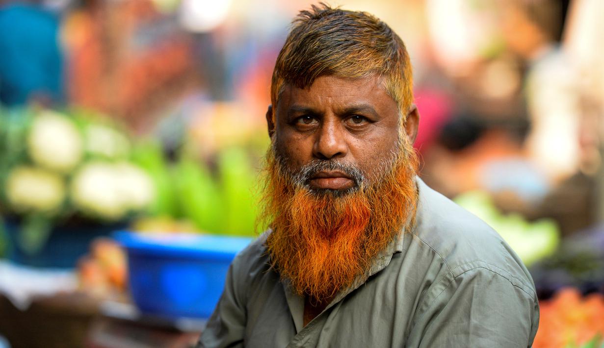 Dalam gambar yang diambil pada 24 Desember 2018, penjual sayur bernama Munir Hossain berpose dengan janggut oranye di Dhaka. Ternyata bukan hanya janggut saja yang mereka warnai, bagian rambut di kepala juga diwarnai dengan henna dan karena banyak yang menggunakannya. (MUNIR UZ ZAMAN / AFP)
