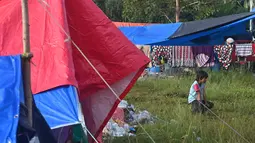 Seorang gadis duduk di antara tenda-tenda saat orang-orang yang terkena dampak tinggal di kamp sementara di Mamuju, Senin (18/1/2021). Gempa berkekuatan magnitudo 6,2 yang terjadi pada Jumat (15/1) dini hari mengakibatkan puluhan orang meninggal dunia. (AFP/Adek Berry)