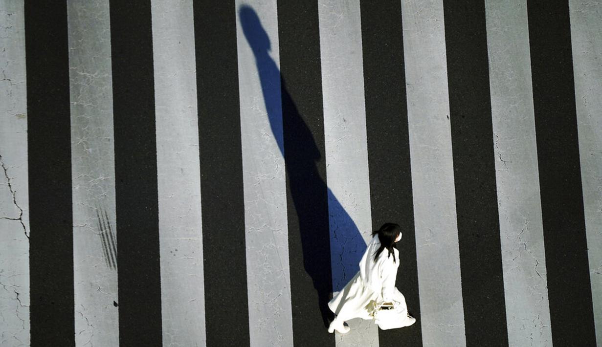 Seorang wanita yang memakai masker untuk membantu mengekang penyebaran COVID-19 menyeberangi jalan di Tokyo, Jepang, 29 Desember 2021. Saat ini, pasien COVID-19 yang dirawat di rumah sakit semakin banyak. (AP Photo/Eugene Hoshiko)