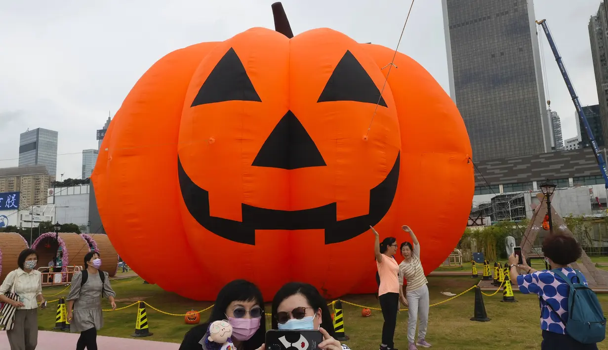 Seorang wanita mengenakan masker untuk mencegah penyebaran virus corona, berpose untuk selfie di depan dekorasi buah labu besar untuk Halloween di sebuah taman di Hong Kong, Rabu (27/10/2021). Tahun ini, perayaan tersebut jatuh pada hari Minggu, 31 Oktober 2021. (AP Photo/Vincent Yu)