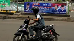 Pengendara sepeda motor melintas di depan spanduk partai yang terpampang di Jalan Sultan Agung, Manggarai, Jakarta, Selasa (16/1). Partai politik menawarkan sembako murah hingga melawan korupsi dalam isi spanduknya. (Liputan6.com/JohanTallo)