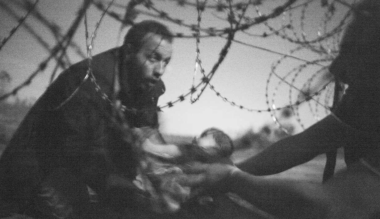 Imigran membawa bayi melewati pagar di perbatasan Roszke, Hongaria, (28/8/20105). Foto kategori World Press Photo of the Year and Spot News karya Warren Richardson berjudul 'Hope for a New Life' menjadi pemenang '1st prize singles'. (Reuters via WPP)