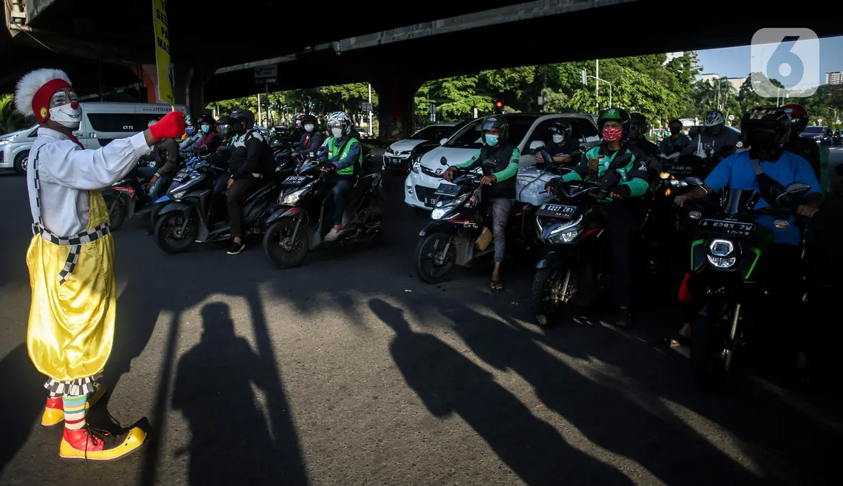 Angggota Komunitas Aku Badut Indonesia (ABI) melakukan aksi kampanye penggunaan di kawasan Cilandak, Jakarta Selatan, Senin (12/7/2021). Selain itu, mereka juga membagi-bagikan masker secara gratis bagi para pengendara motor yang melintas. (Liputan6.com/Johan Tallo)