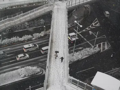 Orang-orang berjalan di atas salju di Tokyo, Kamis (6/1/2022). Badan Meteorologi mengeluarkan peringatan untuk salju lebat di Tokyo pada hari Kamis karena tekanan rendah dan penurunan suhu membawa hujan salju ke area yang luas di pantai Pasifik negara itu. (AP Photo/Koji Sasahara)