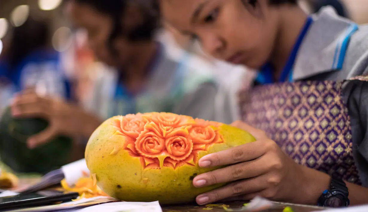 Seorang wanita Thailand mengukir pola bunga pada buah pepaya dalam kompetisi mengukir bunga dan buah di Bangkok, 4 Agustus 2017. Berbekal pisau dan alat bantu lainnya, para peserta mengukir buah dengan tingkat ketelitian tinggi. (Roberto SCHMIDT/AFP)
