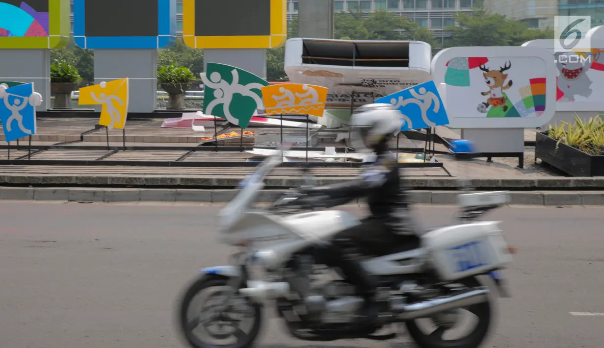 Petugas melintas didepan papan sosialisasi Asian Games 2018 terlihat roboh akibat hujan angin di Bundaran HI, Jakarta, Senin (11/9). (Liputan6.com/Faizal Fanani)