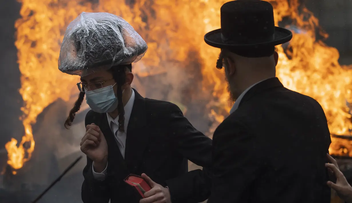 Pria Yahudi Ultra-Ortodoks memakai masker saat membakar beragi sebagai persiapan akhir untuk liburan Paskah di kota Yahudi ultra-Ortodoks Bnei Brak, dekat Tel Aviv, Israel (26/3/2021).  Dalam perayaan ini umat Yahudi dilarang memakan makanan beragi seperti roti tawar. (AP Photo/Oded Balilty)