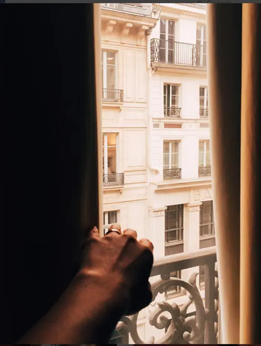 Saat dia mengunggah foto bagian tangan kirinya sedang membuka tirai kamar apartemen hingga terlihat deretan jendela gedung apartemen di luarnya. (Via Instagram/@saputrawijaya)