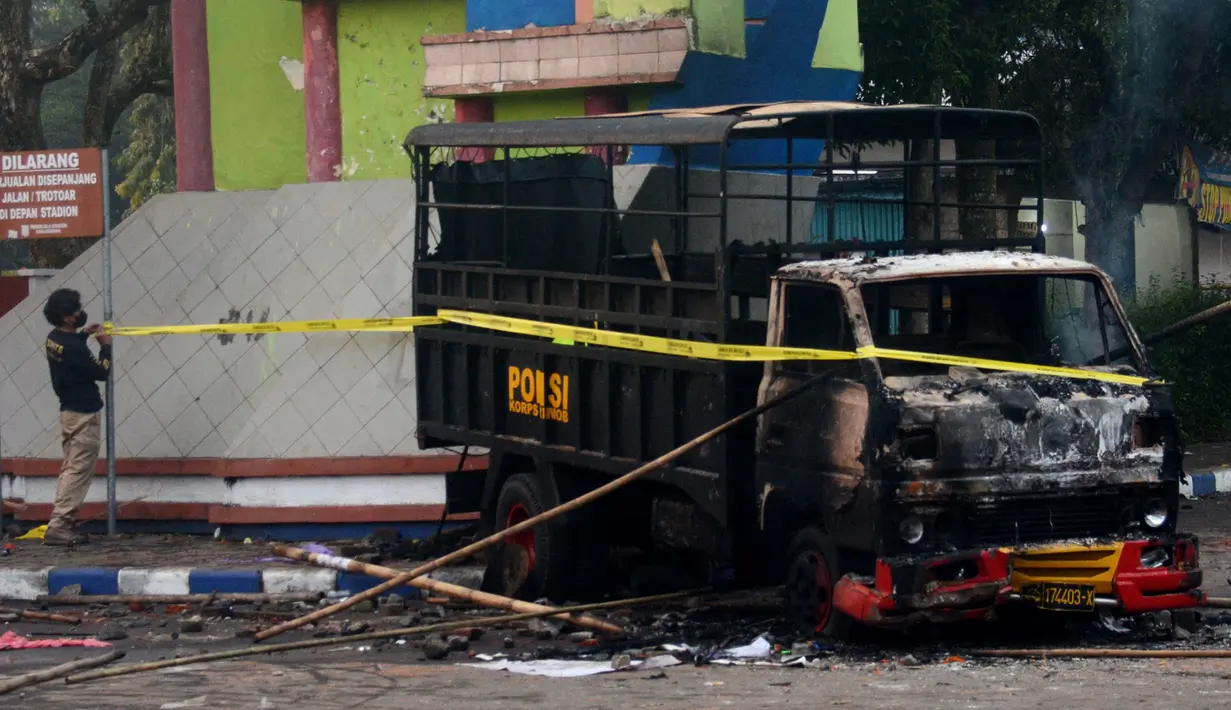 Seorang polisi memasang garis polisi di samping kendaraan yang dibakar di luar Stadion Kanjuruhan, Malang, Jawa Timur, Minggu (2/10/2022). Sebanyak 127 orang tewas ketika para penggemar yang marah menyerbu lapangan sepak bola setelah pertandingan antara Arema FC dan Persebaya Surabaya pada 1 Oktober 2022. (PUTRI/AFP)