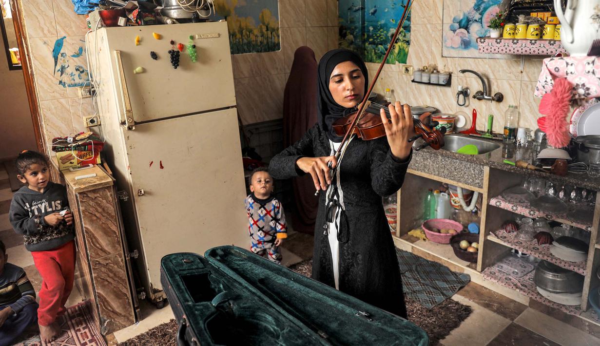 Musisi Palestina Jawaher al-Aqraa memainkan biola sambil berdiri di dapur rumahnya di Deir al-Balah, Jalur Gaza Tengah, 24 Oktober 2023. (Eyad BABA/AFP)