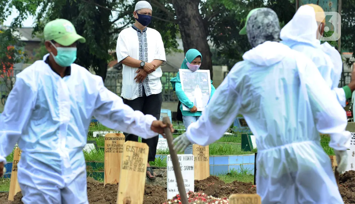 Seorang pria dan anak perempuan menyaksikan pemakaman jenazah korban COVID-19 di TPU Tegal Alur, Jakarta, Kamis (17/12/2020). Hingga hari ini, intensitas pemakamanan korban covid-19 di DKI masih tinggi dengan rata-rata yang dimakamkan mencapai 30 hingga 38 jenazah per hari. (merdeka.com/Arie basuki)