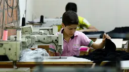 Bocah pengungsi Suriah bernama Muhamed saat menjahit kain di sebuah pabrik tekstil, Istanbul, Turki, (24/6). Meski seumurannya masih menikmati bangku sekolah, mereka menikmati pekerjaan mereka. (REUTERS/Murad Sezer)