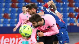 Striker Levante, Enis Bardhi (atas) berebut bola dengan bek Barcelona, Gerard Pique dalam laga lanjutan Liga Spanyol 2020/2021 pekan ke-36 di Ciutat de Valencia Stadium, Valencia, Selasa (11/5/2021). Levante bermain imbang 3-3 dengan Barcelona. (AFP/Jose Jordan)