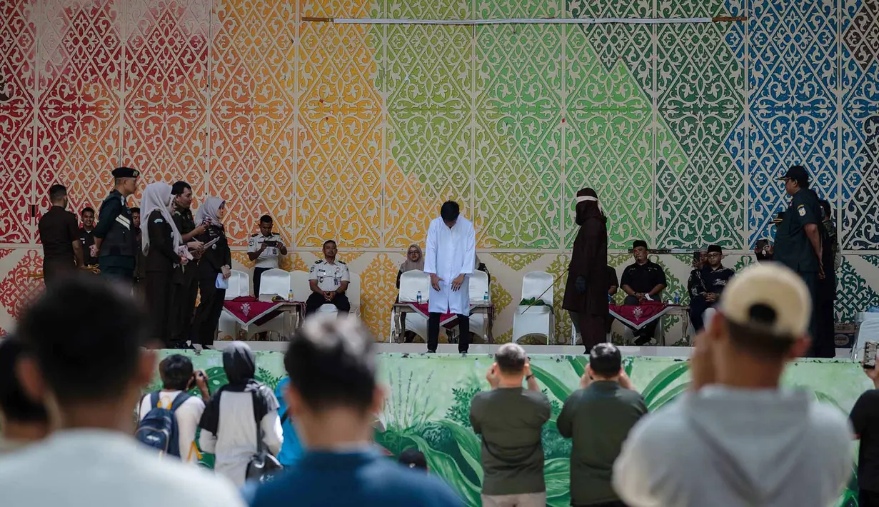 Warga menyaksikan saat algojo mengeksekusi cambuk terhadap terpidana pelanggar hukum syariat Islam, diantaranya karena mencium seorang wanita saat siaran langsung TikTok, menjalani hukuman cambuk di Taman Bustanussalatin, Banda Aceh, Aceh, Kamis (2/7/2026). (AP Photo/Reza Saifullah)