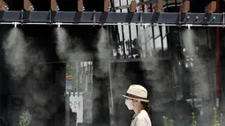 Seorang wanita berjalan di bawah titik kabut yang menyejukkan di sepanjang jalan di Tokyo, Selasa (10/8/2021). Menurut biro meteorologi Jepang, cuaca panas panas terus berlanjut di wilayah metropolitan saat suhu naik menjadi 338 derajat Celcius (100,4 derajat Fahrenheit). (AP Photo/Eugene Hoshiko)