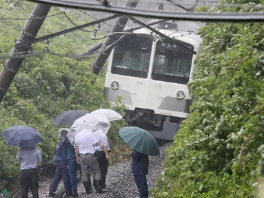 Petugas mengamati kereta yang tergelincir dalam tanah longsor yang disebabkan topan mindulle di Higashimurayama, Tokyo, Senin (22/8). Ratusan penerbangan serta perjalanan kereta api di Tokyo dibatalkan akibat terjangan Topan Mindulle. (Jiji Press/AFP)