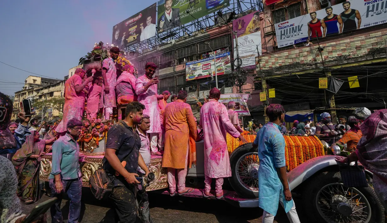 Umat Hindu berkerumun di sekitar mobil Rolls Royce 1921 yang dimodifikasi membawa patung dewa Krishna melalui bangunan bersejarah Howrah Bridge selama festival Holi di Kolkata, India, Minggu, 5 Maret 2023. (AP Photo/Bikas Das)