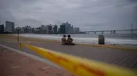 Sepasang kekasih duduk di pantai yang ditutup di kawasan pejalan kaki di pantai Gwangalli di Busan (2/9/2020). Penerbangan dihentikan di Korea Selatan dan peringatan badai dikeluarkan di kedua sisi semenanjung Korea sebagai topan yang diperkirakan akan menjadi salah satu yang terkuat. (AFP/Ed Jones)