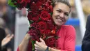 Petenis Rumania, Simona Halep memeluk buket bunga berbentuk angka satu saat merayakan kemenangan atas Jelena Ostapenko (Latvia) pada semifinal China Terbuka 2017 di Beijing, Sabtu (7/1). Halep naik ke posisi teratas WTA kali pertama. (GREG BAKER / AFP)