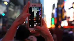 Seorang wanita mengambil gambar fenomena Manhattanhenge, dimana matahari terbenam sejajar tepat dengan jalan, di Times Square, New York City, Kamis (12/7). Manhattanhenge dimana saat matahari terbenam sejajar dengan jalan. (AFP/TIMOTHY A. CLARY)