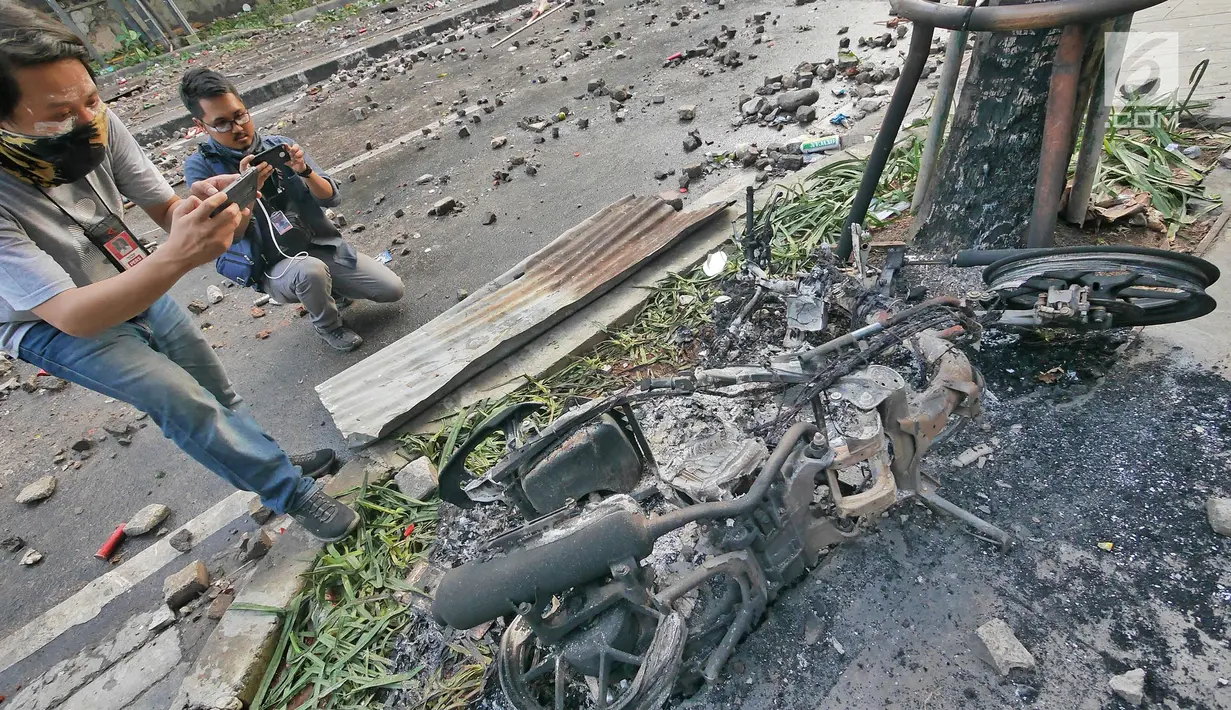 Dua orang pria mengambil gambar bangkai motor yang dibakar oleh massa aksi 22 Mei di sekitaran Jakarta, Kamis (23/5/2019). Aksi unjuk rasa itu dilakukan menyikapi putusan hasil rekapitulasi nasional Pemilu serentak 2019. (Liputan6.com/Herman Zakharia)