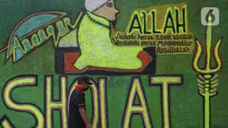 Warga berjalan di depan mural bernuansa Islami di Gang Pelangi, kawasan Kalibata, Jakarta, Jumat (23/4/2021). Mural bernuansa Islami tersebut dibuat warga untuk menghiasi dan meramaikan pintu masuk gang dalam rangka menyambut bulan Ramadhan. (Liputan6.com/Herman Zakharia)
